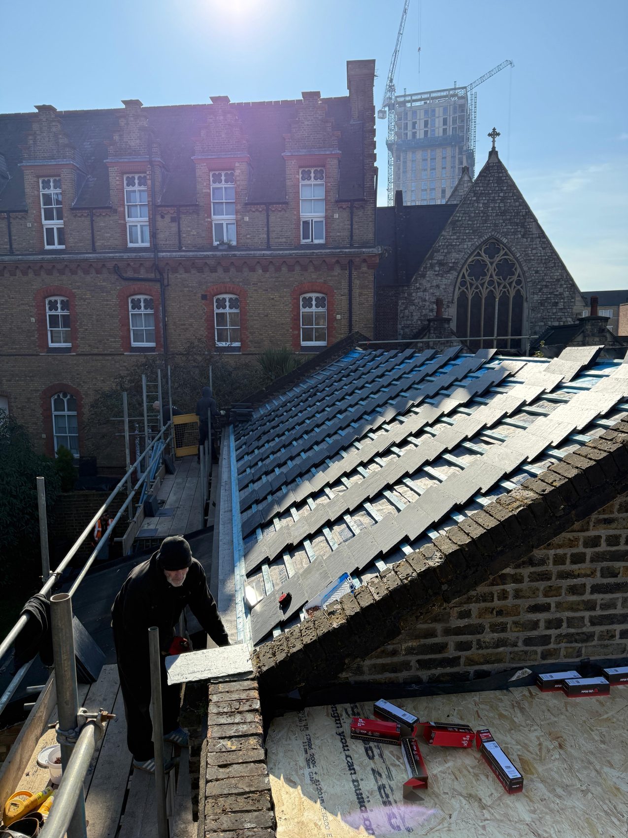 Natural slate being laid back over new battens and underlay beside the relined parapet gutter, Gothic church behind