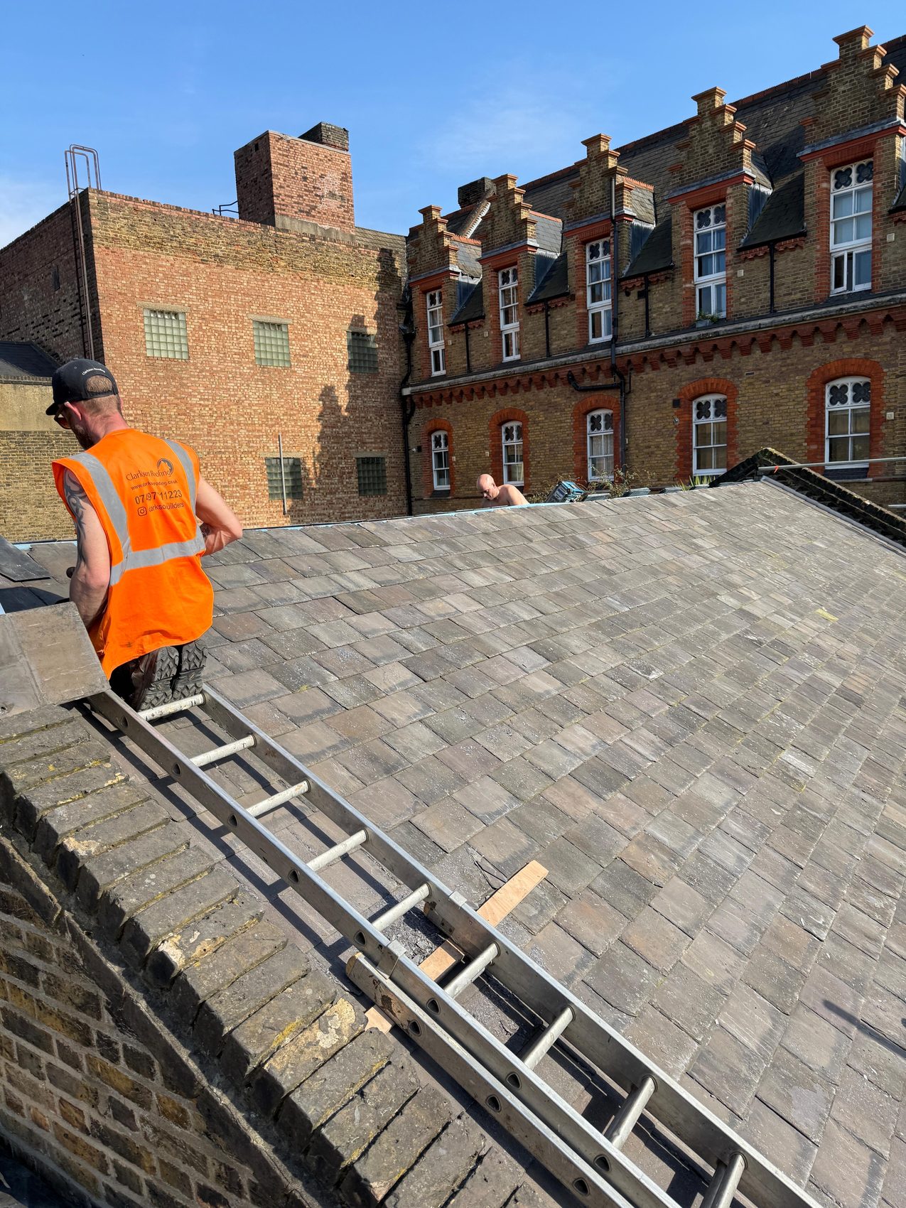 Clarkson Roofing worker climbing a roof ladder up the completed natural slate roof, heritage red-brick range behind