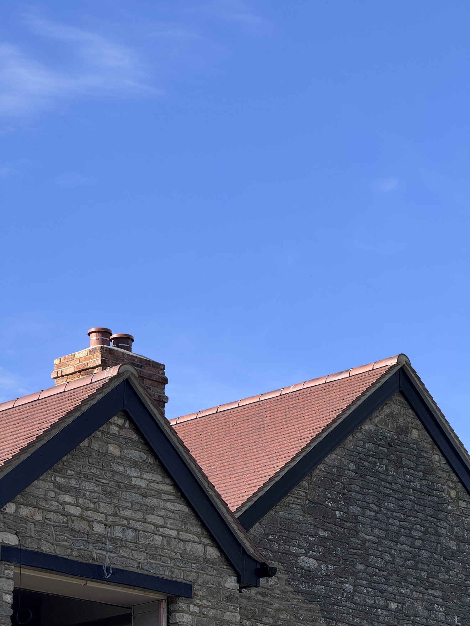 Twin-gable stone property re-roofed in clay tile with a rebuilt chimney
