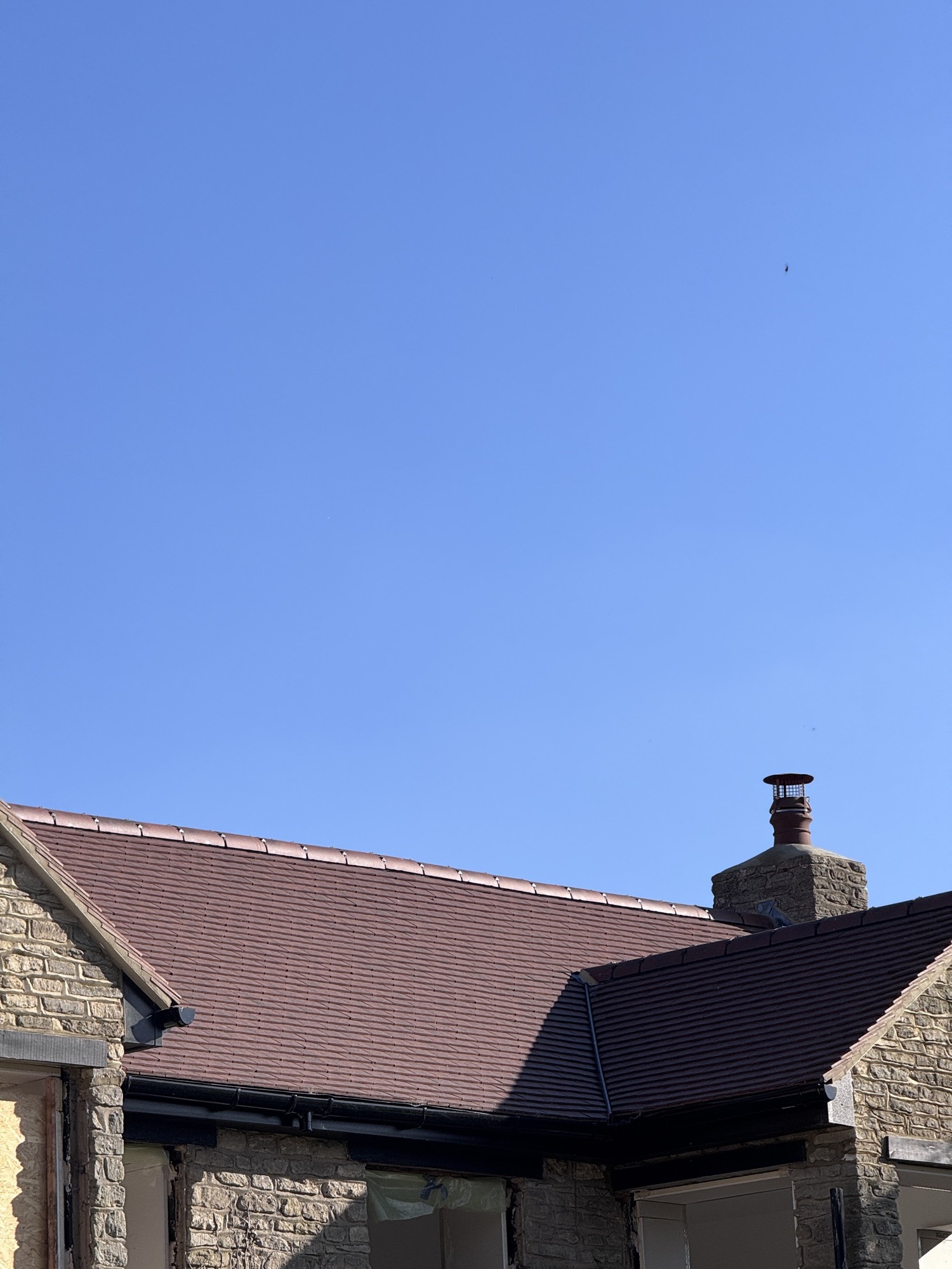 Clay plain-tile roof with a new stone chimney against a blue sky