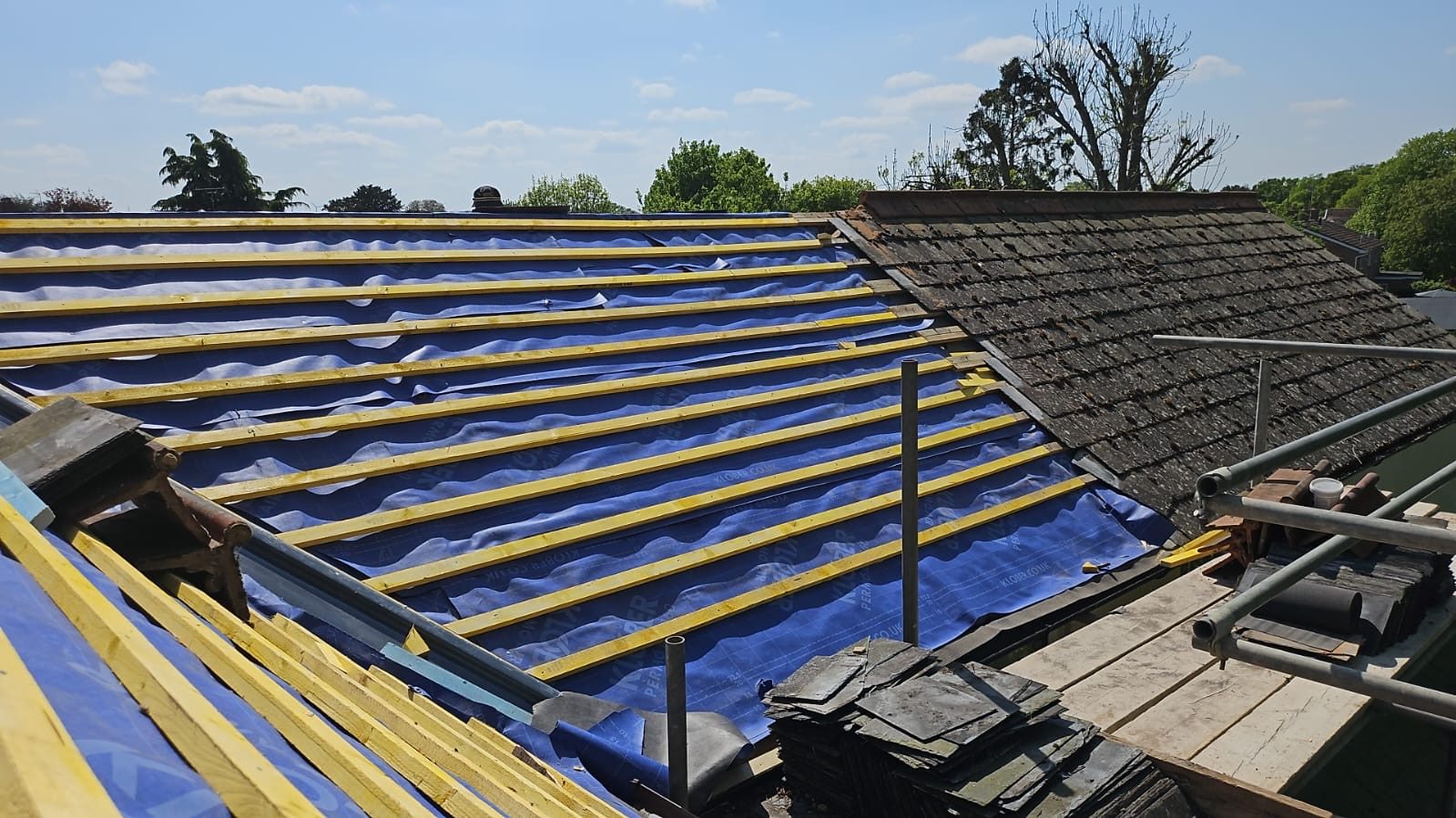 Old dark roof covering being stripped on the right, with new breathable felt and battens going on to the left